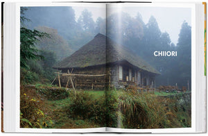 Traditional Japanese thatched roof farmhouse surrounded by lush greenery.